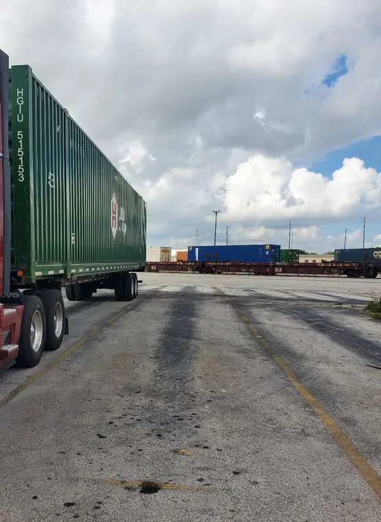 Green container on a chassis at an intermodal yard with loaded railcars behind