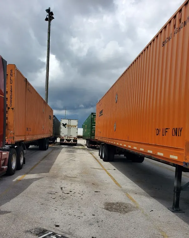 Orange intermodal containers on chassis lined up in a rail yard under storm clouds