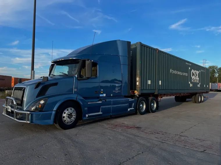 Blue Volvo tractor pulling a CSX container