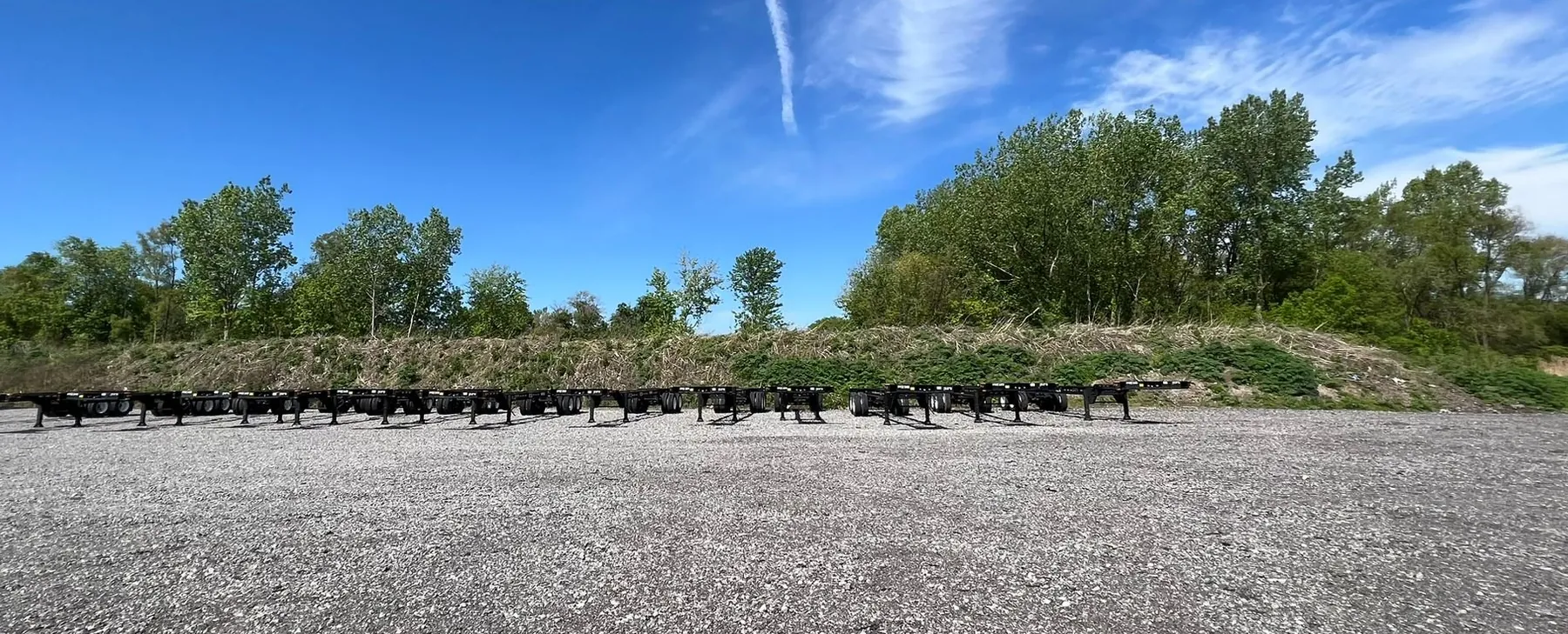 Row of empty container chassis parked in a gravel yard